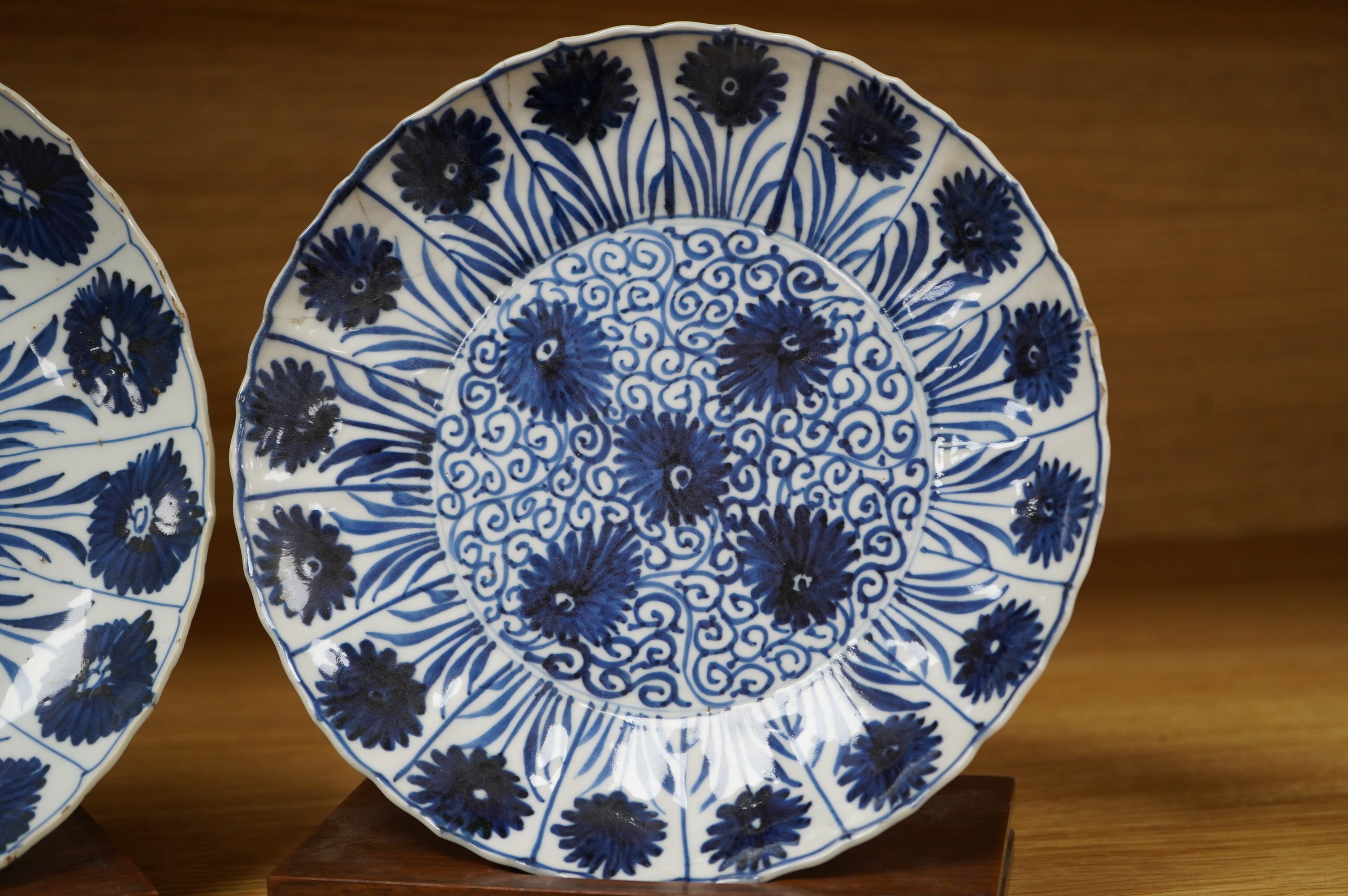 Two Chinese blue and white ‘astor’ plates, Kangxi period, with hardwood stands, largest 22cm diameter. Condition - poor to fair